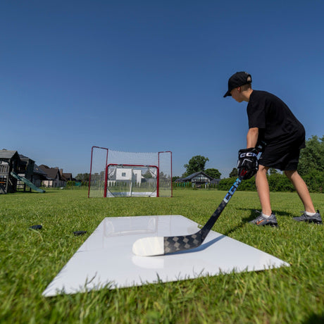 Hockey player winding up for a shot from a shooting pad in the garden with a net in the background