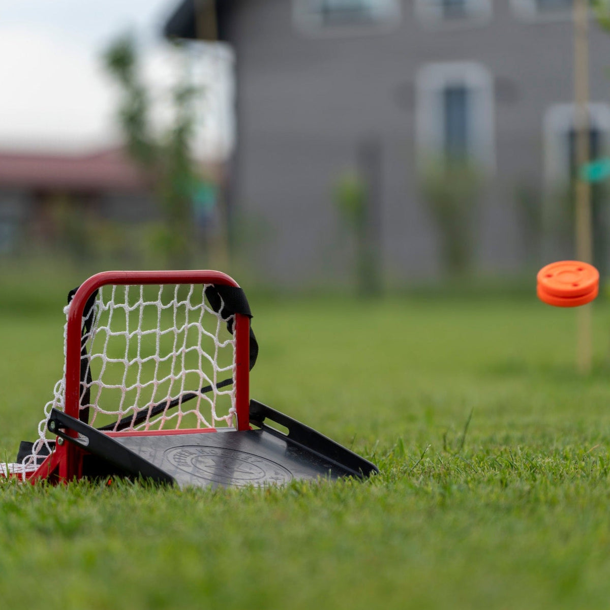 Hockey sauce catcher set up on a garden lawn with orange puck flying toward the net