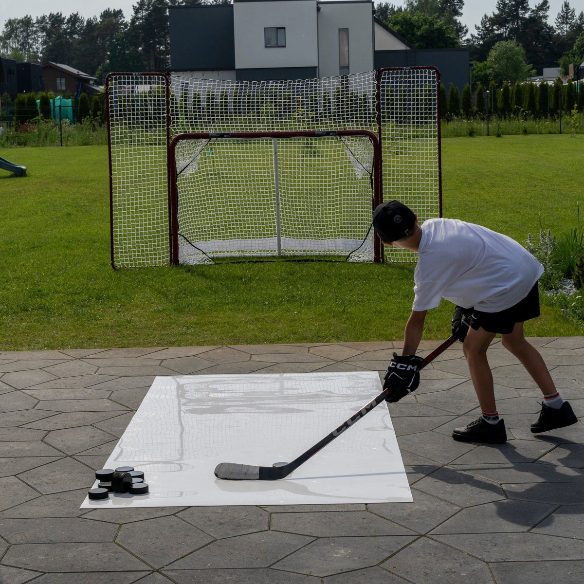 Young hockey player shooting pucks from a roll-up shooting pad toward a net in the garden
