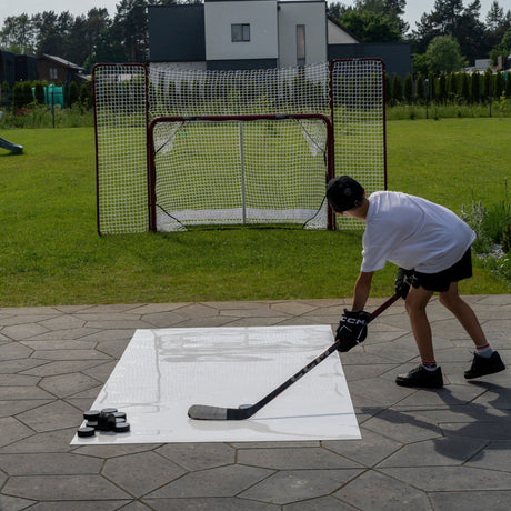 Young hockey player shooting pucks from a roll-up shooting pad toward a net in the garden