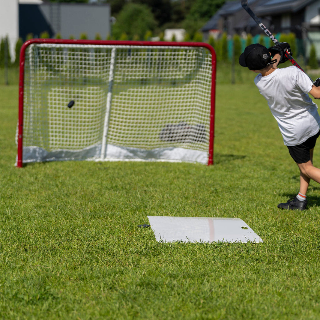 Young hockey player shooting a puck at a full-size goal in the garden