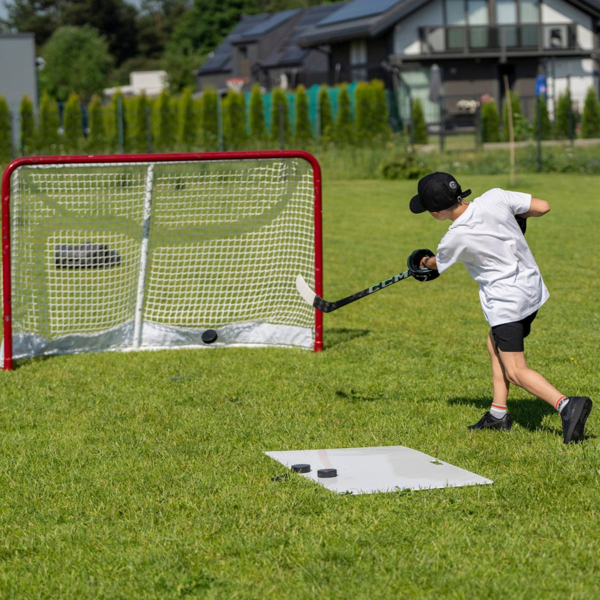 Young hockey player shooting pucks in the garden on a Better Hockey shooting pad