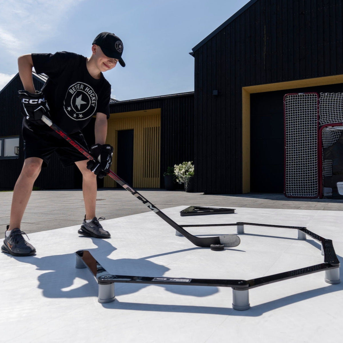 Young hockey player in Better Hockey shirt training with a stickhandling trainer on an outdoor court